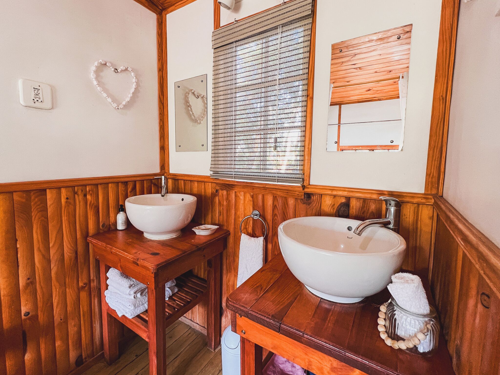 A wooden bathroom with two sinks, a mirror, and a window with blinds.
