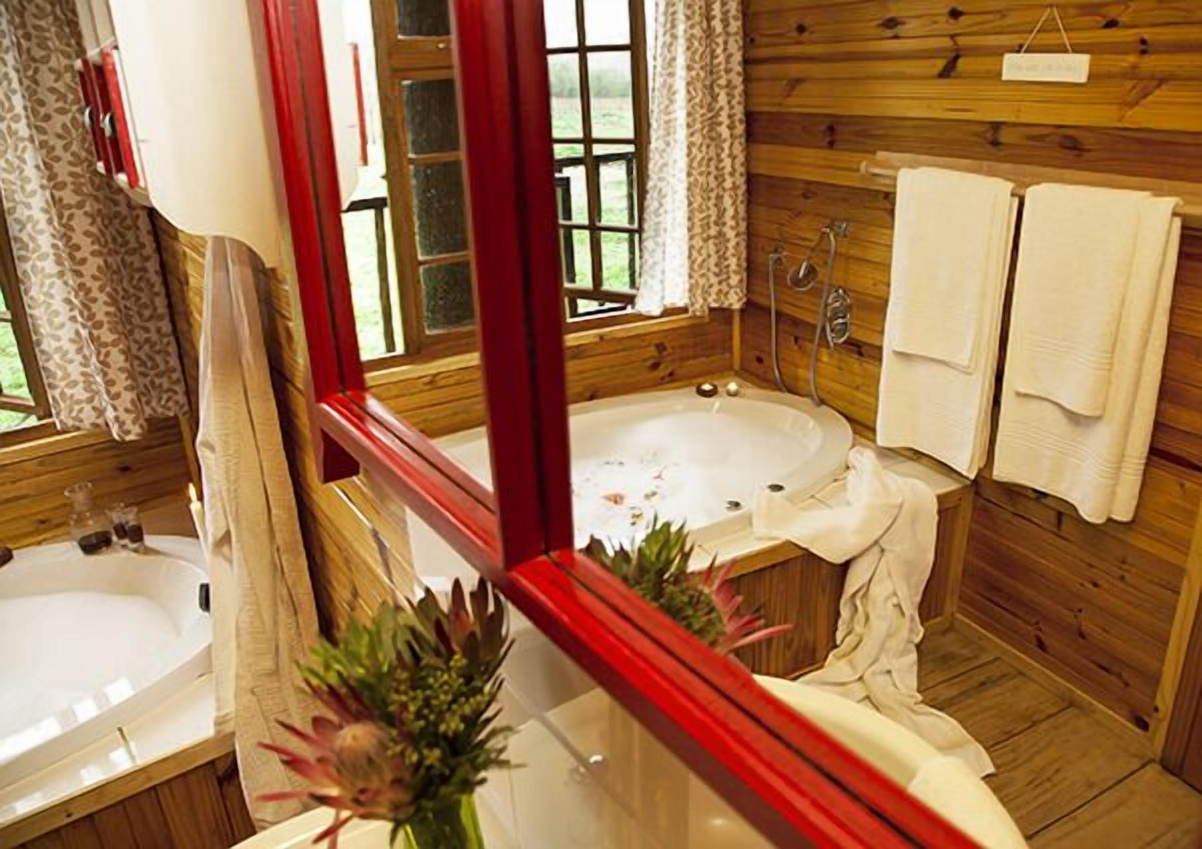 A wooden cabin bathroom with a large bathtub, a sink, and a mirror.