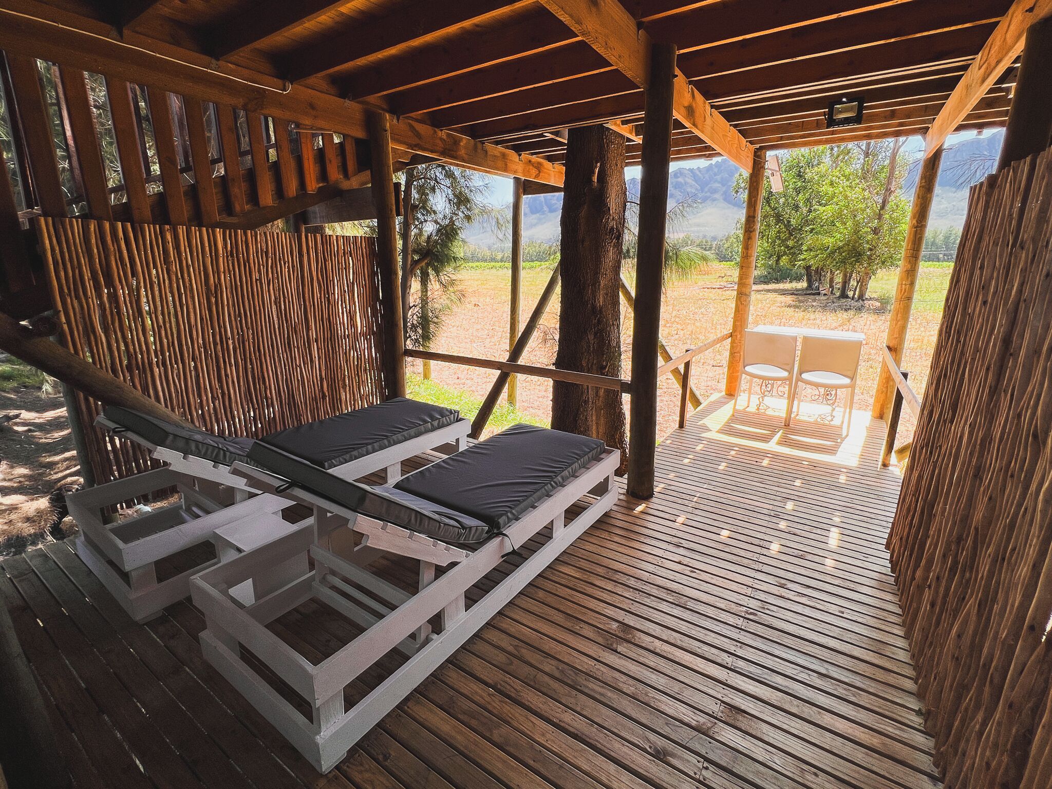 A wooden deck with two lounge chairs and a table, overlooking a mountainous landscape.