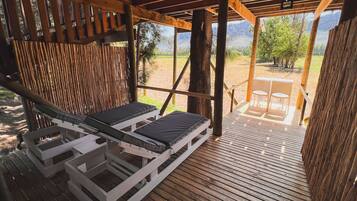 A wooden deck with two lounge chairs and a table, overlooking a mountainous landscape.