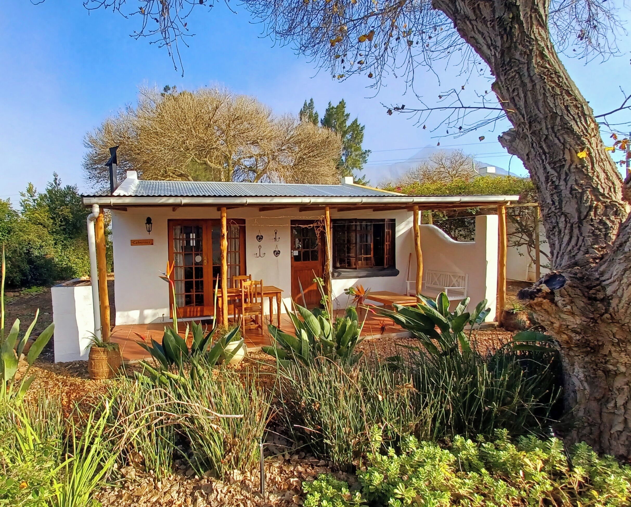 Un piccolo cottage bianco con tetto in tegole, mobili in legno e un giardino antistante.