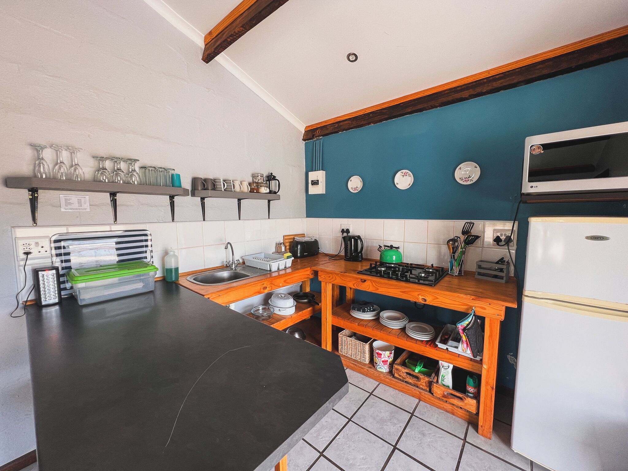 A compact kitchen with a black countertop, wooden shelves, a gas stove, and a white refrigerator.