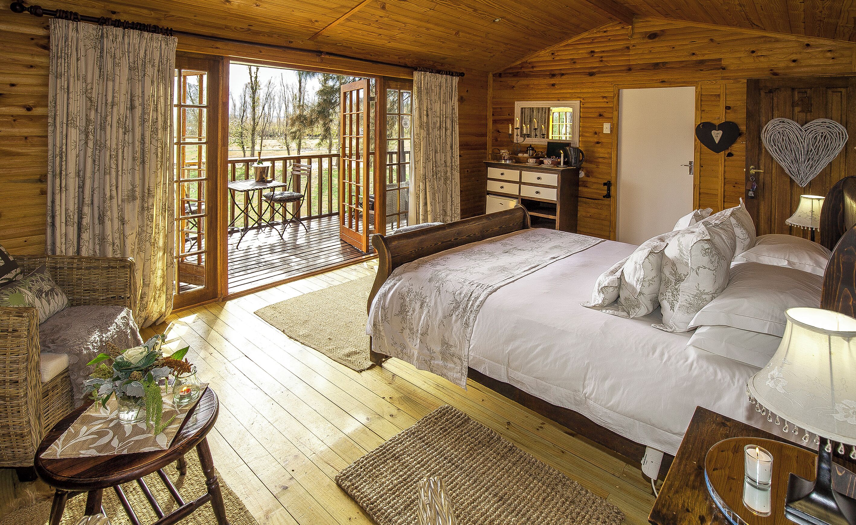 Um quarto de cabana de madeira aconchegante, com uma cama grande, uma escrivaninha de madeira e uma varanda com mesa e cadeiras.