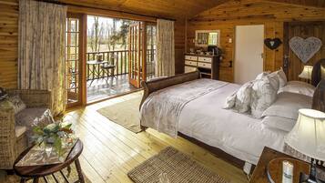 Um quarto de cabana de madeira aconchegante, com uma cama grande, uma escrivaninha de madeira e uma varanda com mesa e cadeiras.