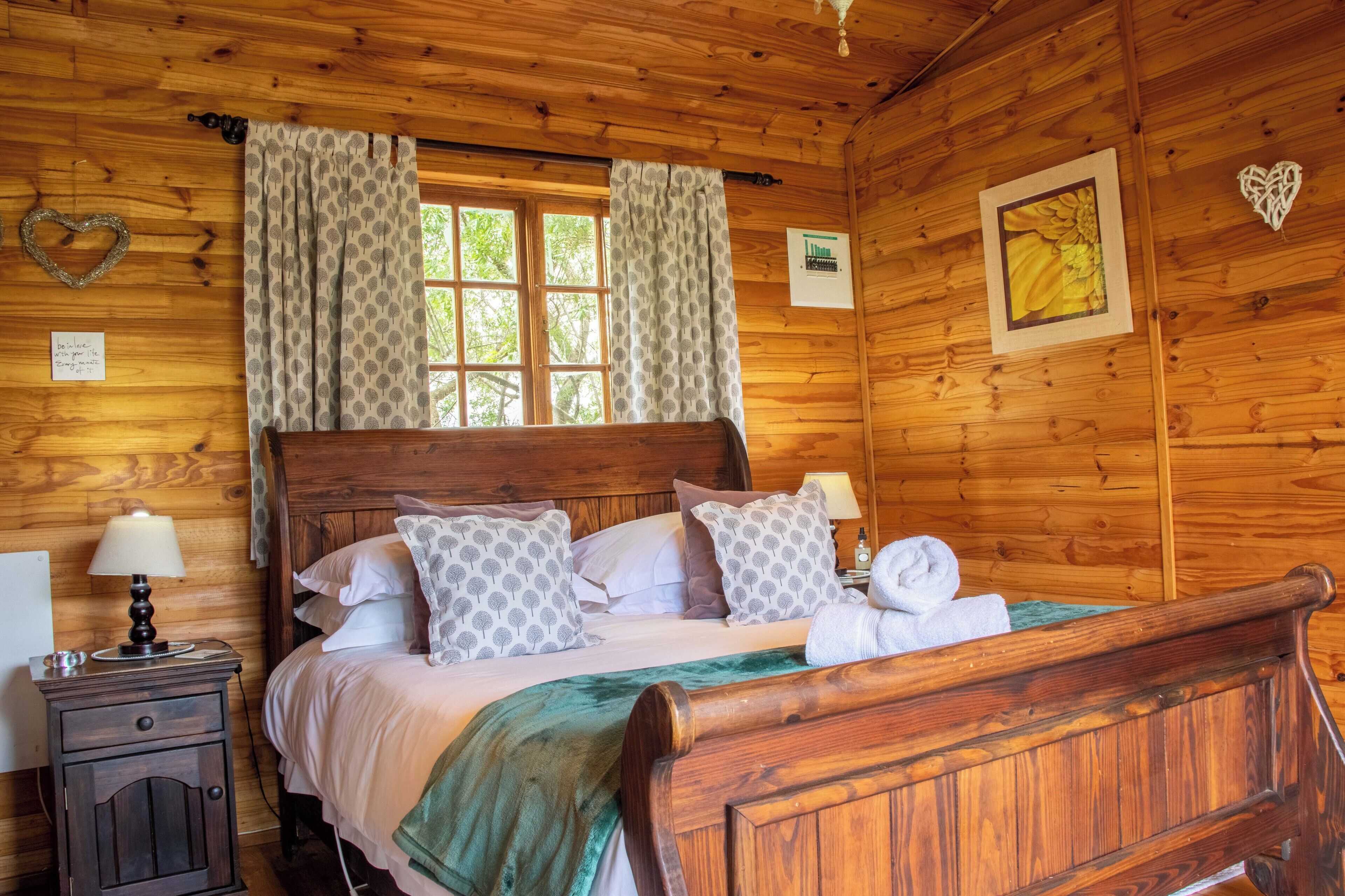 Ein holzgetäfelter Raum im Chalet-Stil mit einem hölzernen Bett, Vorhängen, einem Nachttisch und einem an der Wand hängenden Bild.