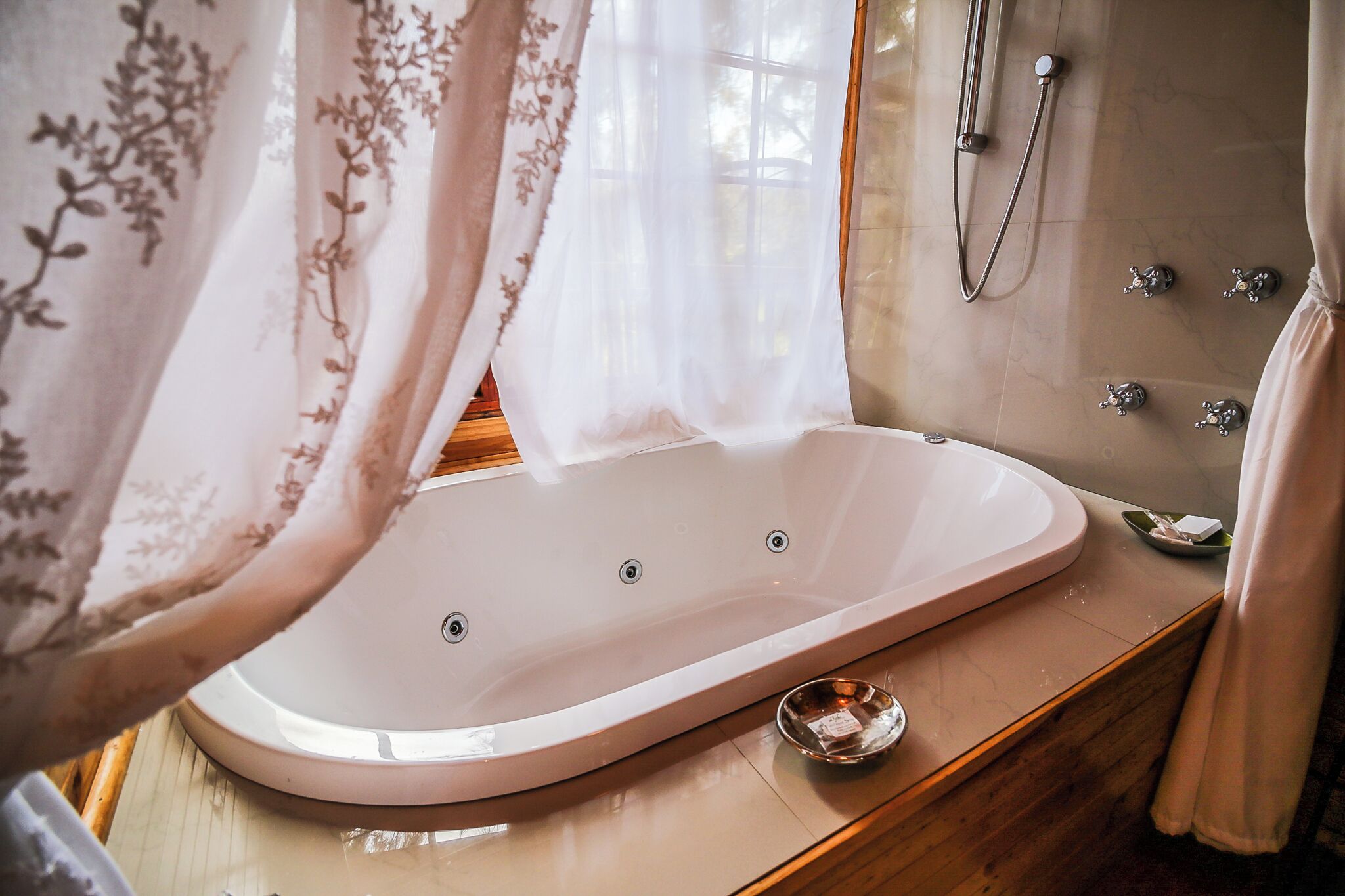 Une salle de bain avec une baignoire sur pieds, une pomme de douche et un lavabo muni d’un porte-savon.