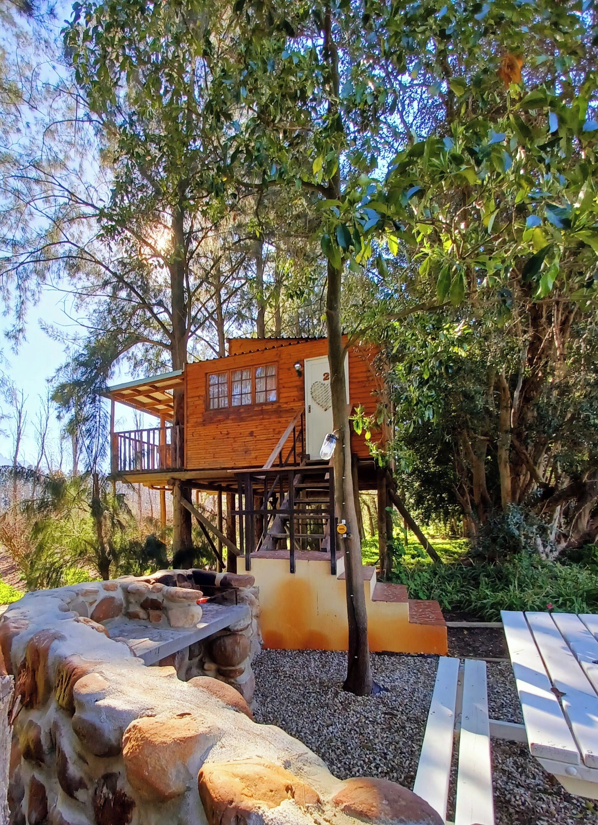 A wooden cabin with a balcony, surrounded by trees and a stone wall.