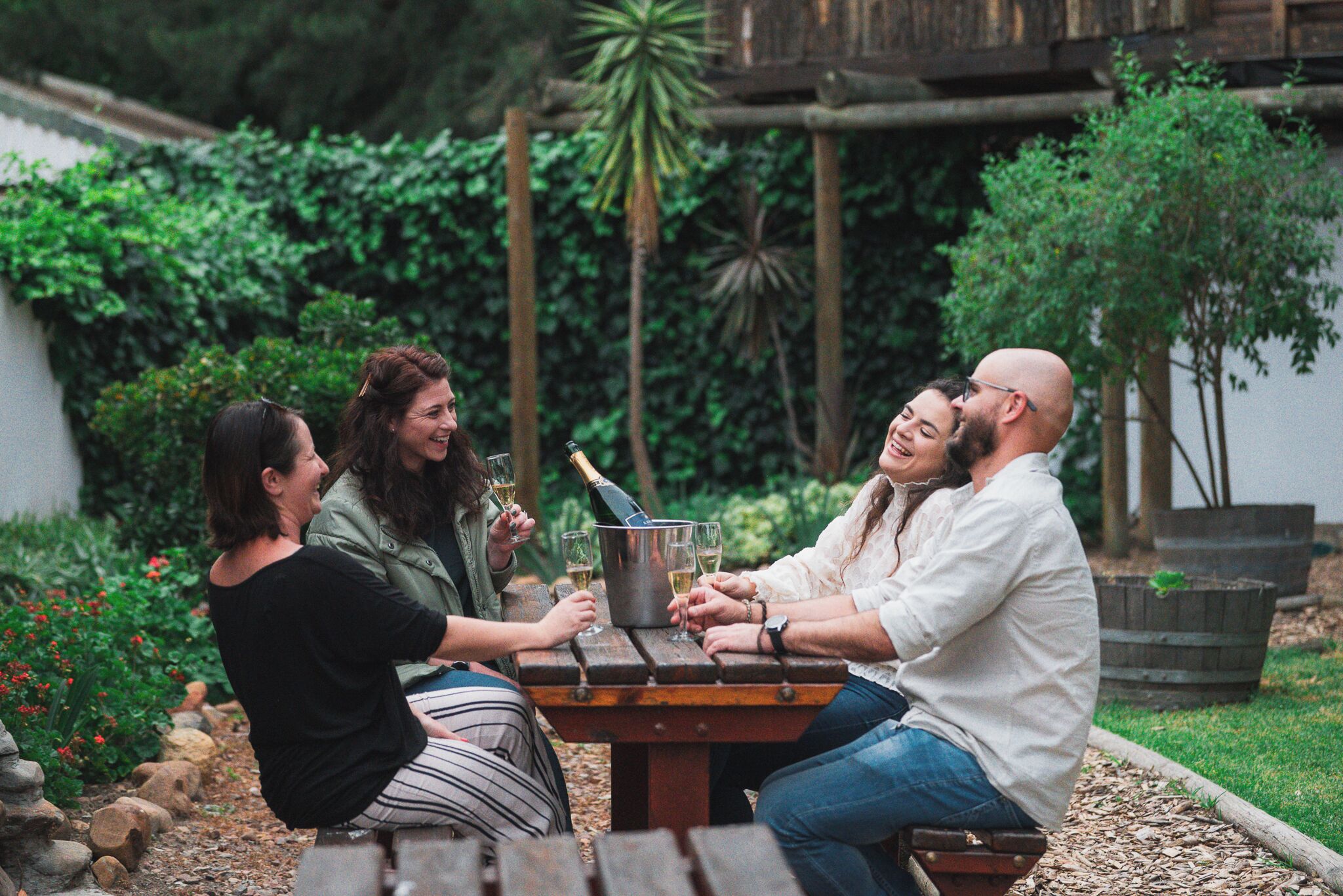 Tres personas sentadas en una mesa de madera al aire libre, con follaje en el fondo.