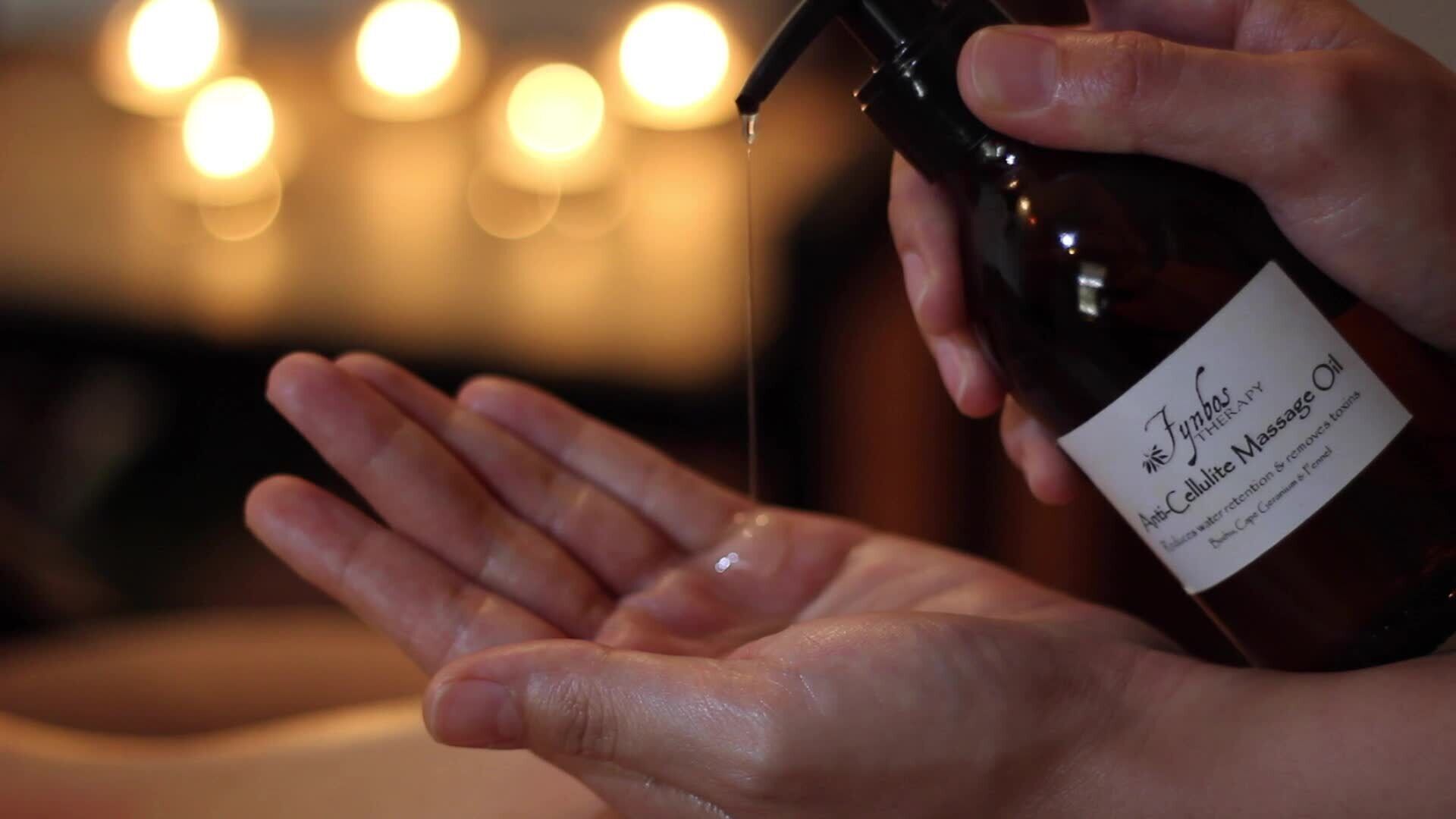 A hand holding a bottle of massage oil.