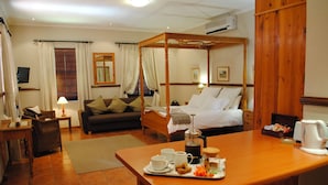 Een hotelkamer met een hemelbed, een eettafel met ontbijtartikelen, een bank en een bijzettafeltje.