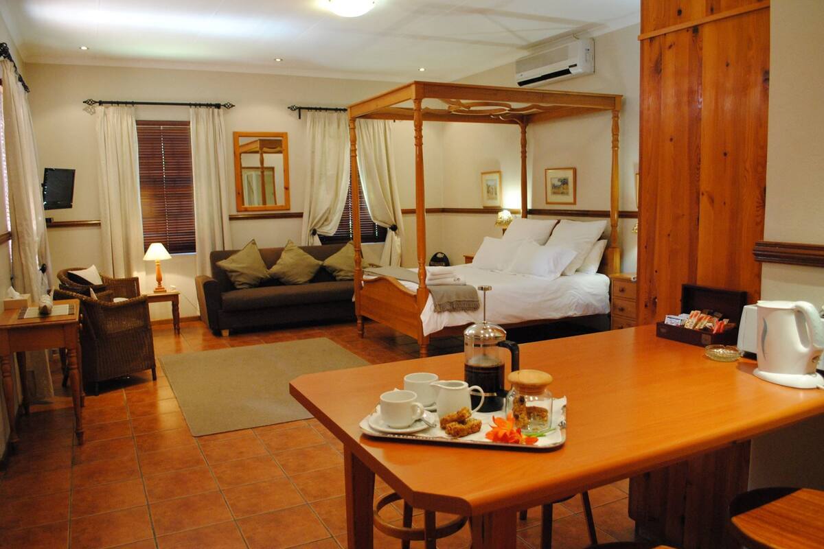 A hotel room with a four-poster bed, a dining table with breakfast items, a sofa, and a coffee table.