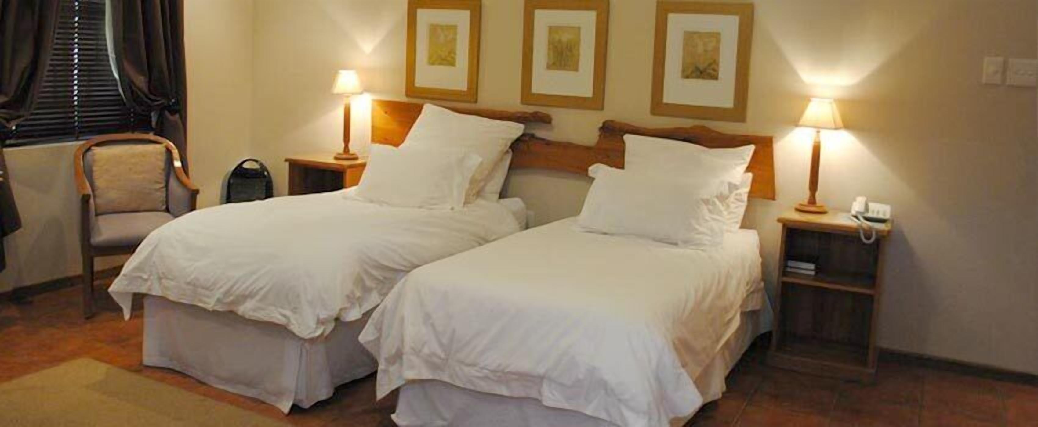 Quarto de hotel com duas camas de solteiro, uma cadeira e mesas de cabeceira com luminárias.