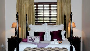Una cama con dosel en tonos blanco y morado, dos mesitas de noche con lámparas, y una ventana con persianas.