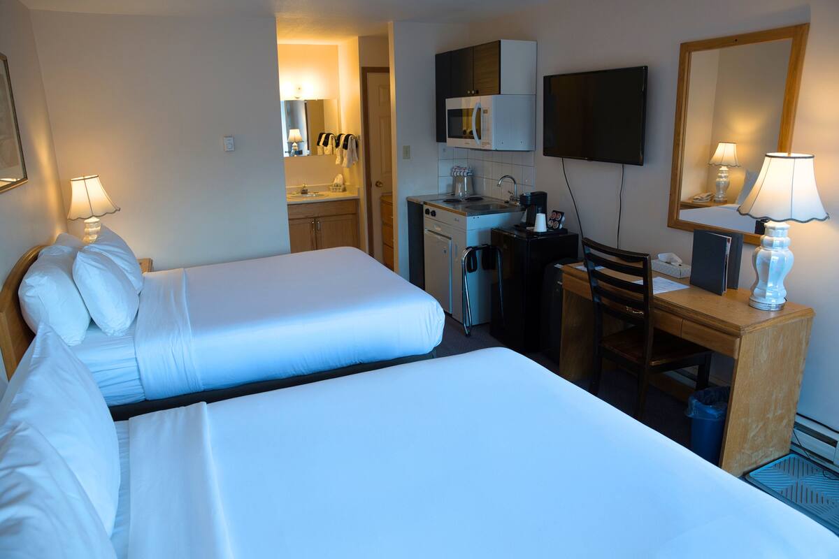 Habitación de hotel con dos camas, un escritorio, una silla, microondas, cafetera y televisor.