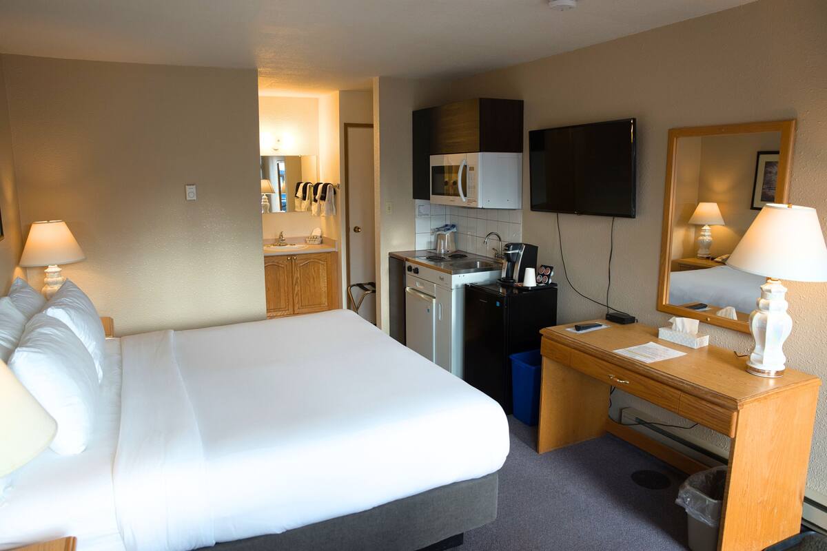 Habitación de hotel con cama, escritorio, microondas, televisión y una pequeña kitchenette.