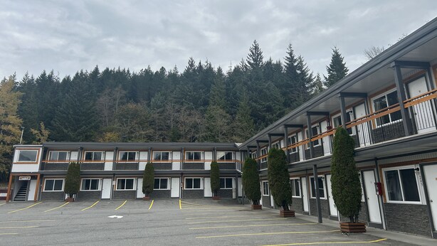 A multi-story hotel with a parking lot, surrounded by trees and a forested hillside. - Chalet Inn (Kitimat)