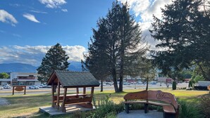 A wooden gazebo and a bench in a park with a parking lot and buildings in the background. - Chalet Inn (Kitimat)
