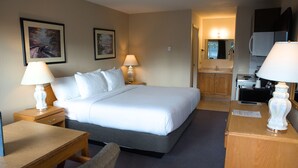 A hotel room with a bed, bedside tables, a desk, and a kitchenette. - Chalet Inn (Kitimat)