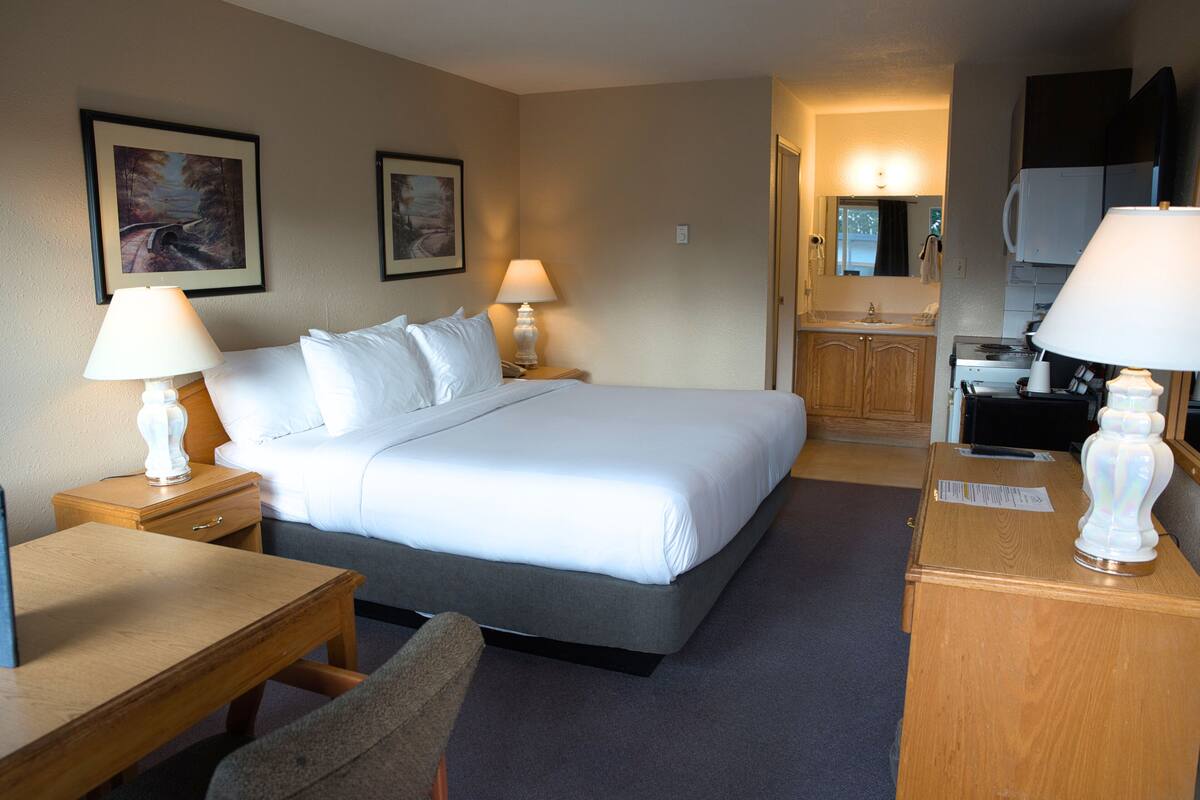Una habitación de hotel con cama, mesitas de noche, escritorio y kitchenette.