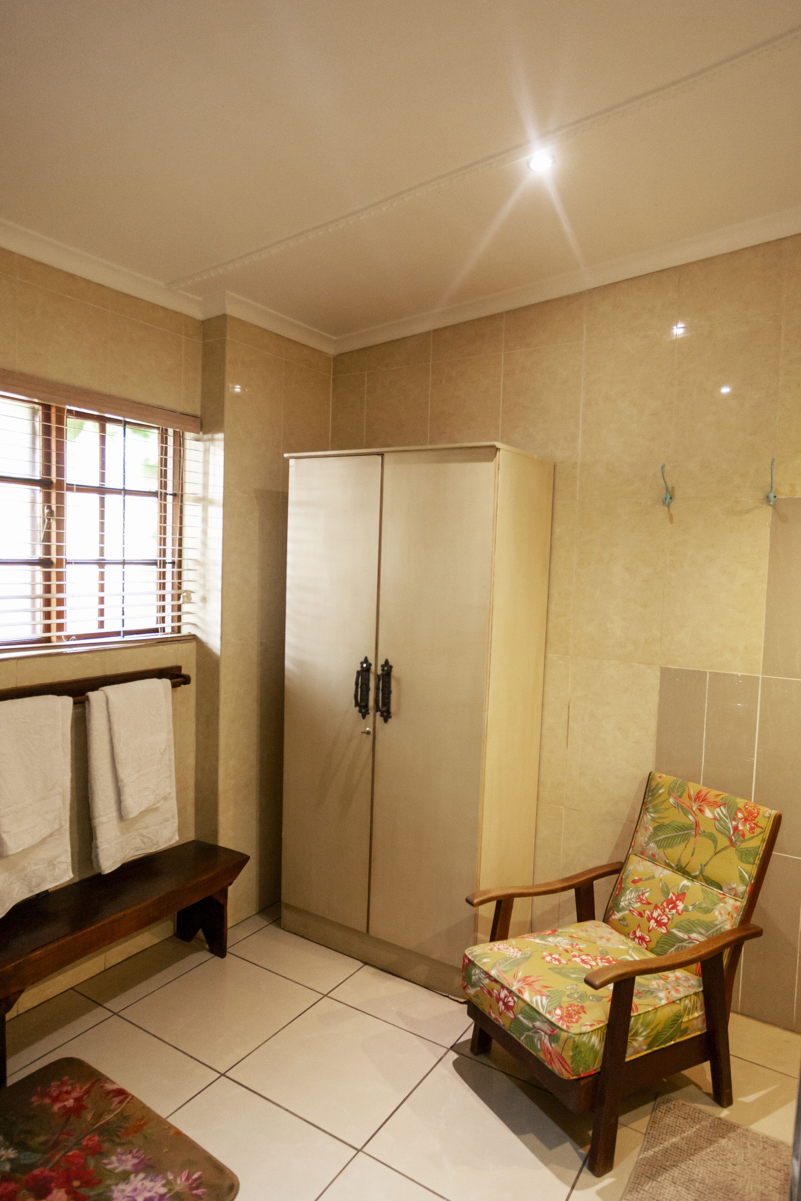 Une salle de bain avec un banc en bois, un meuble et une chaise à motifs floraux.