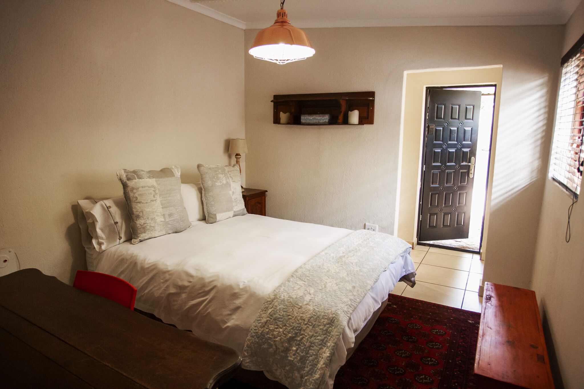 Un dormitorio con cama, mesita de noche, lámpara y una puerta con ventanal.