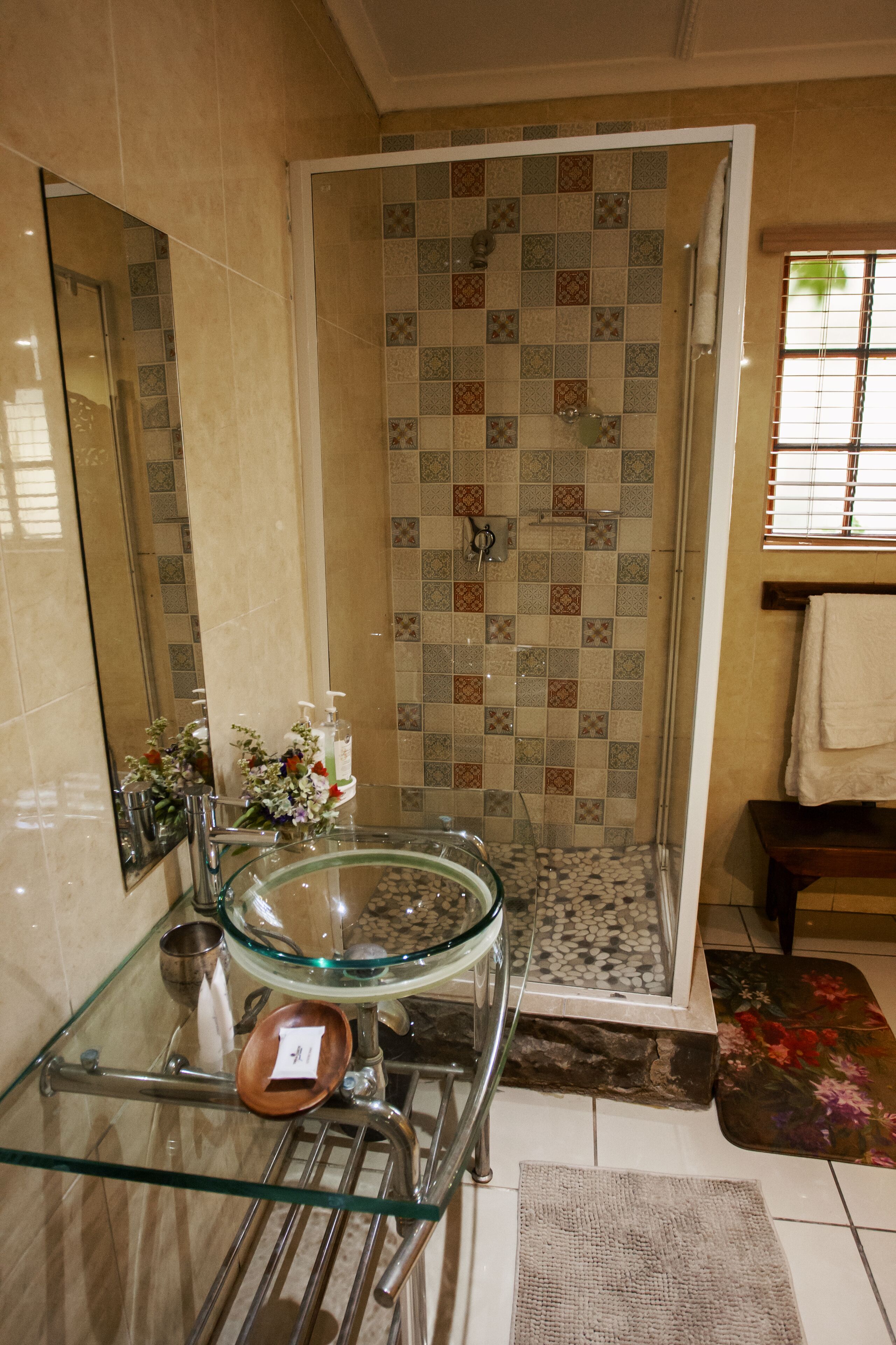 Uma casa de banho com lavatório de vidro, chuveiro com azulejos estampados e espelho.