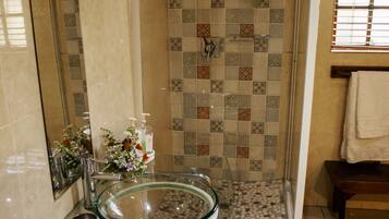 Uma casa de banho com lavatório de vidro, chuveiro com azulejos estampados e espelho.