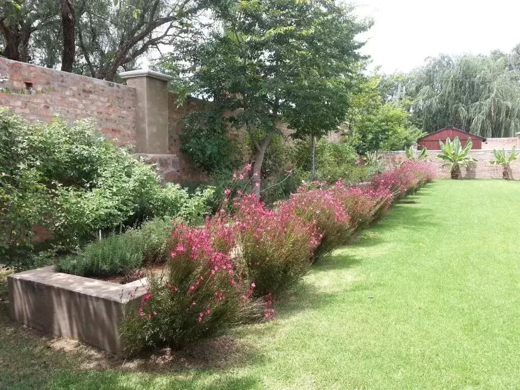 A well-maintained garden with a brick wall, flowering bushes, and a lawn.