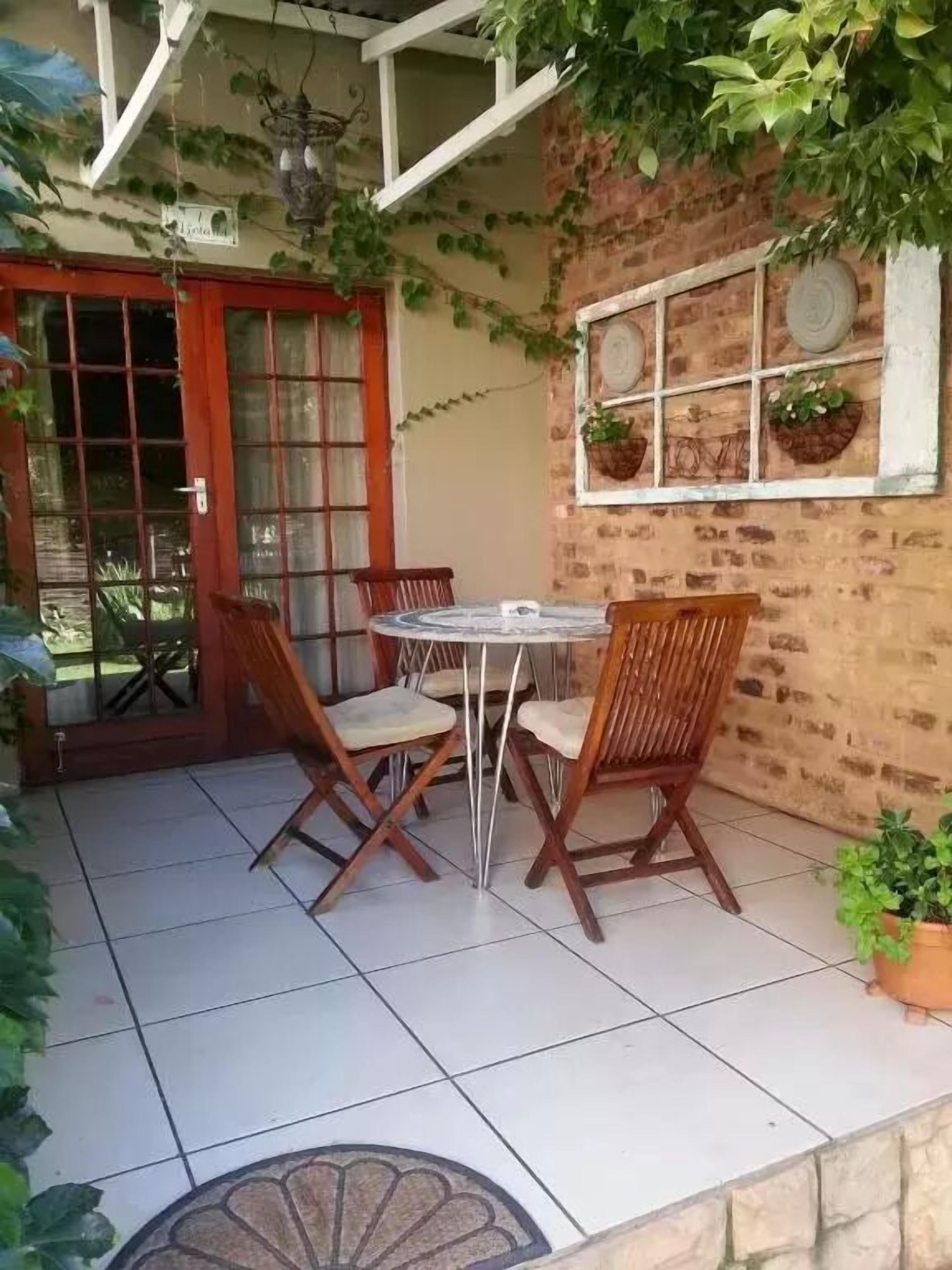 Un patio con una mesa redonda y cuatro sillas de madera, un muro de ladrillo y una ventana decorada.
