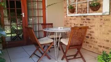 Un patio con una mesa redonda y cuatro sillas de madera, un muro de ladrillo y una ventana decorada.