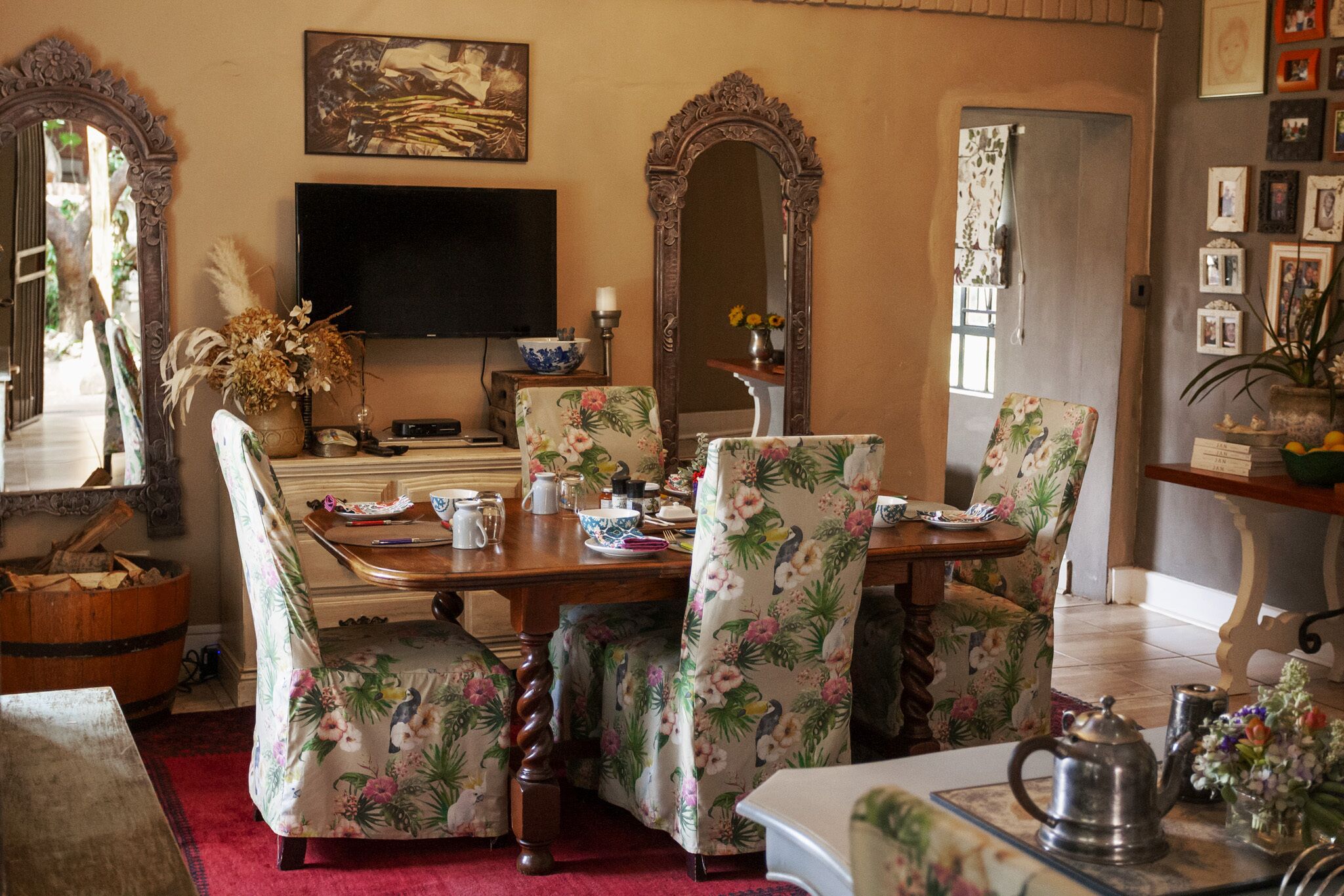 A dining area with a wooden table, floral chairs, a television, and a mirror.