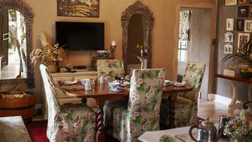 A dining area with a wooden table, floral chairs, a television, and a mirror.