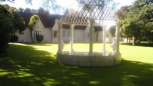 A gazebo with a circular base and a lattice roof, surrounded by a well-maintained lawn and trees. - Victorian Guest House (Krugersdorp)