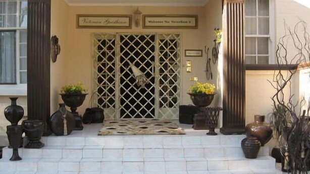 A hotel entrance with a white lattice door, potted plants, and a tiled entrance area. - Victorian Guest House (Krugersdorp)