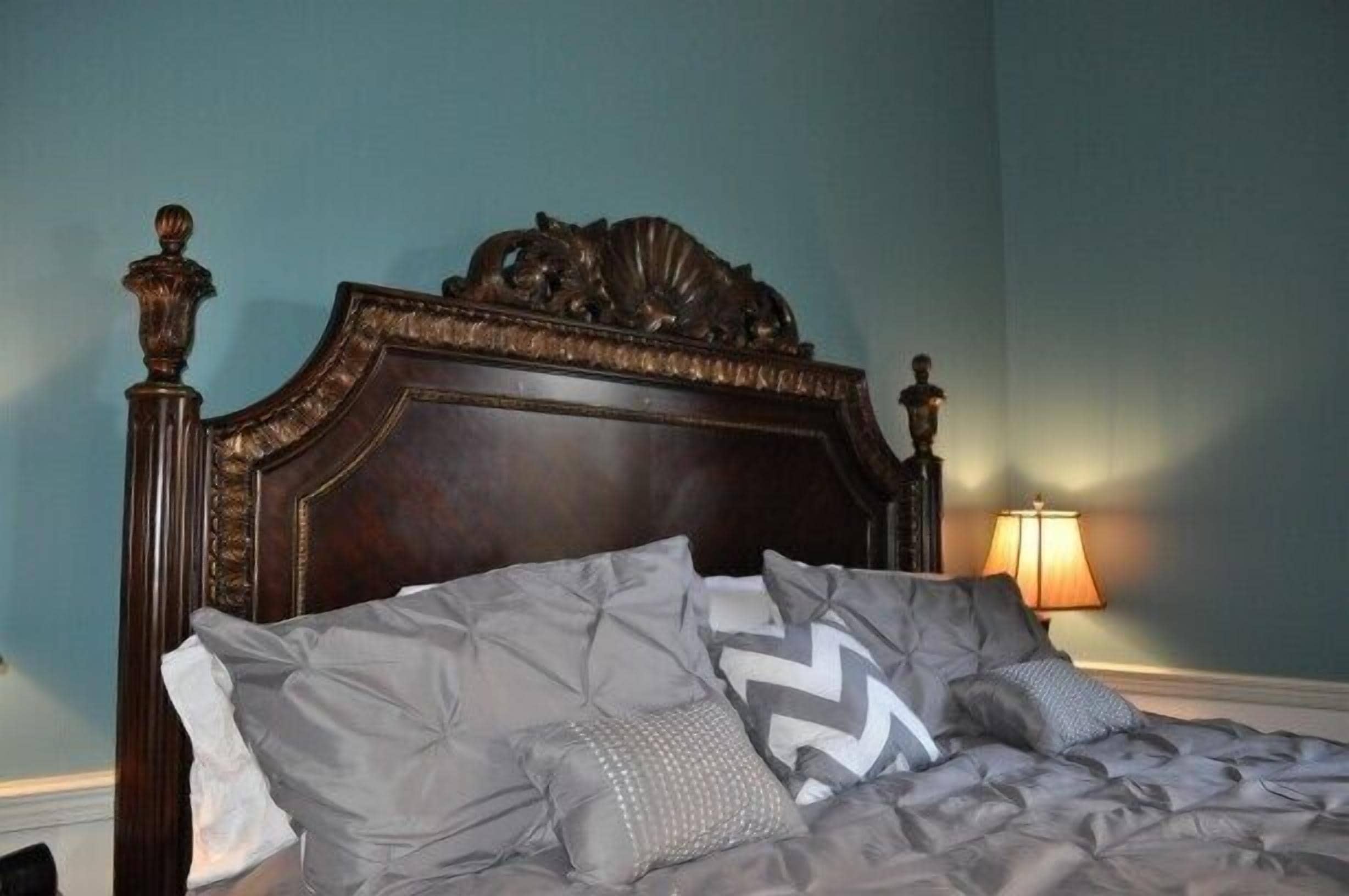 A bed with a dark wooden headboard and grey bedding.