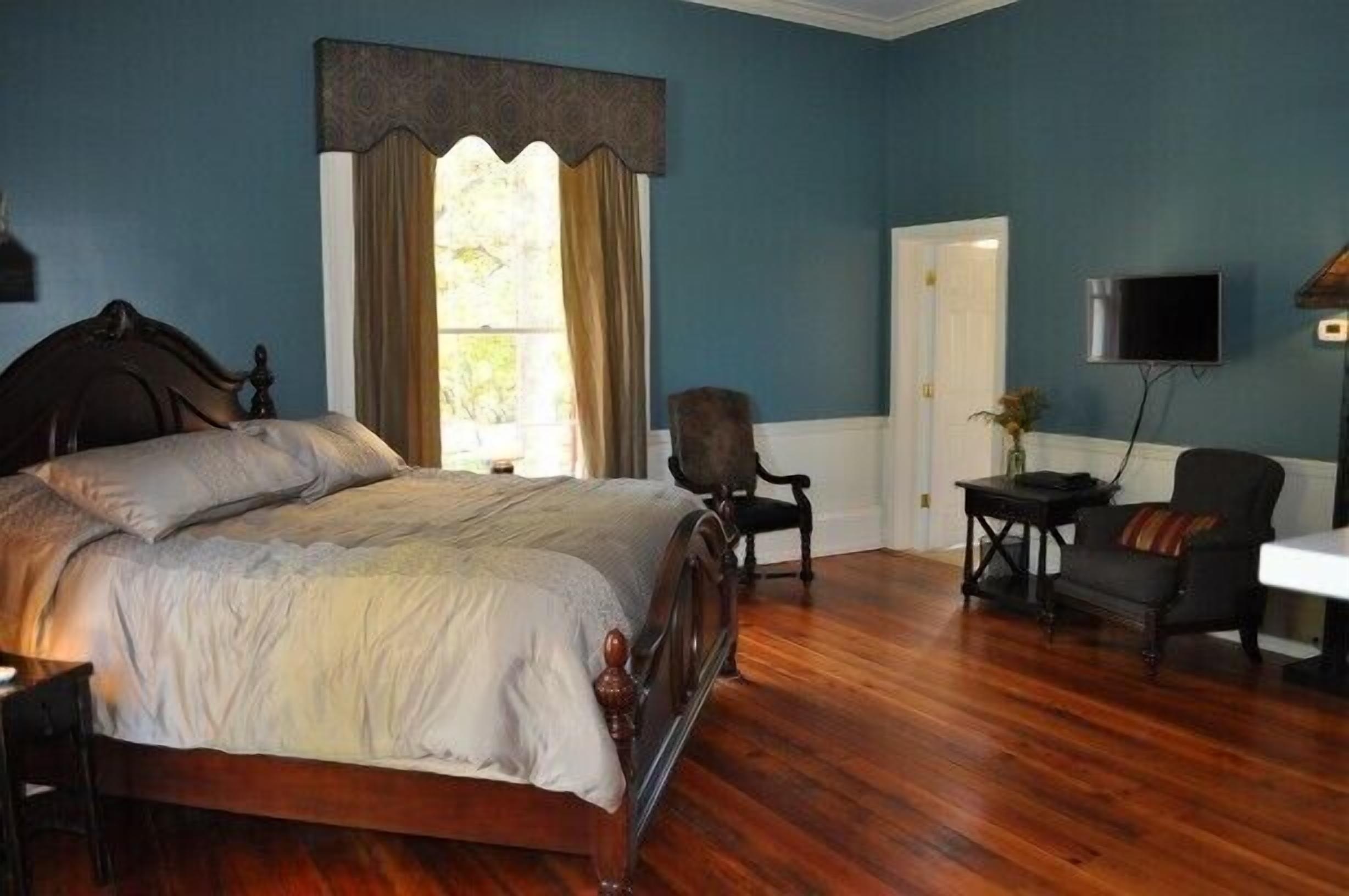 A bedroom with a large bed, a chair, a small table, and a television.