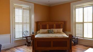 A bedroom with a wooden bed, two windows with shutters, and a ceiling fan.