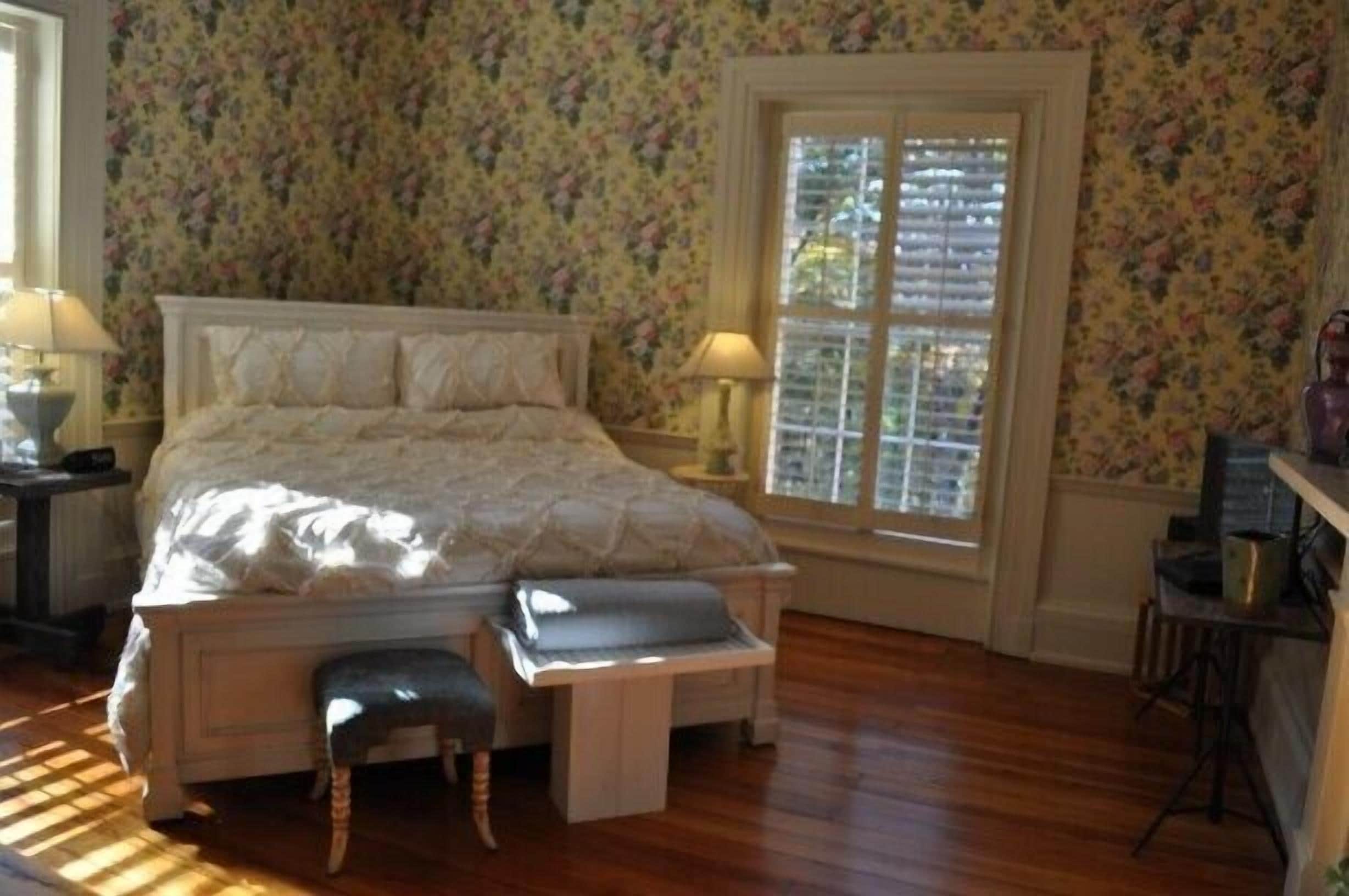 A bedroom with a bed, a bench, a window, and a nightstand.