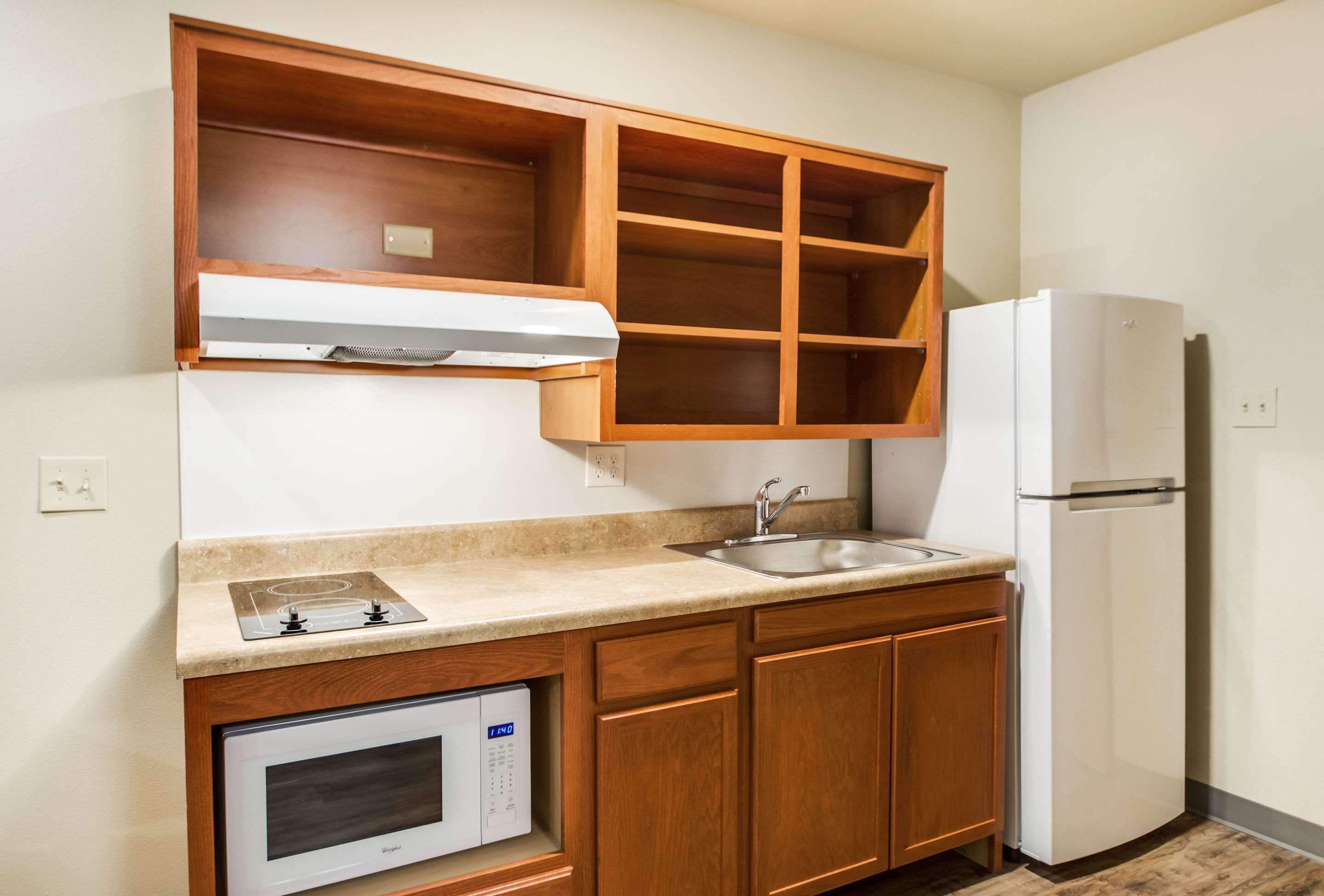 A compact kitchen with wooden cabinets, a built-in microwave, a gas stove, a sink, and a refrigerator.