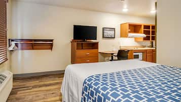 Quarto de hotel com cama, televisão, escrivaninha com cadeira, micro-ondas e guarda-roupa.