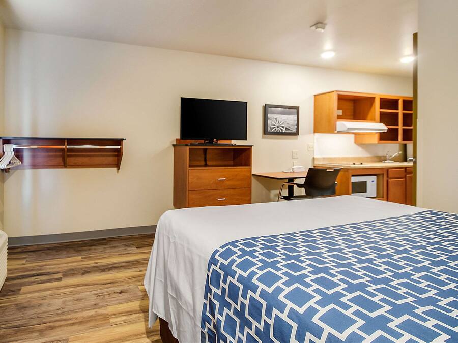 Quarto de hotel com cama, televisão, escrivaninha com cadeira, micro-ondas e guarda-roupa.