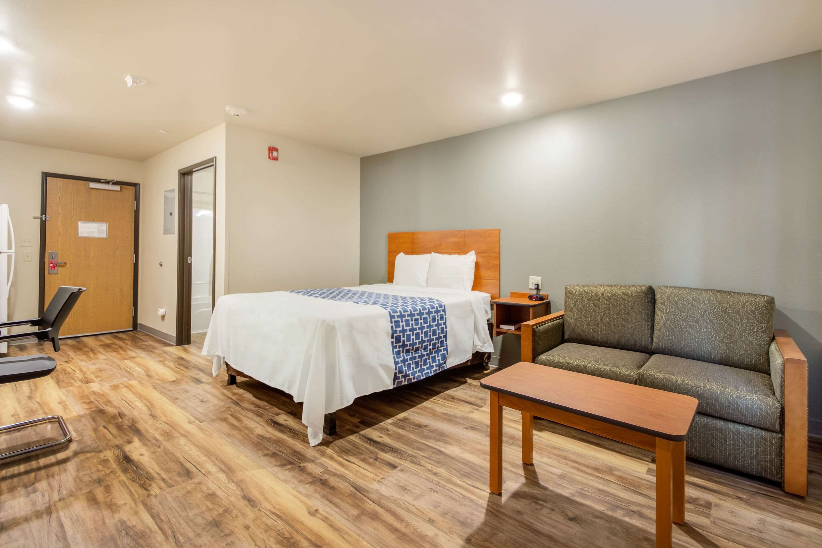 A hotel room with a bed, a sofa, a small table, and a treadmill.