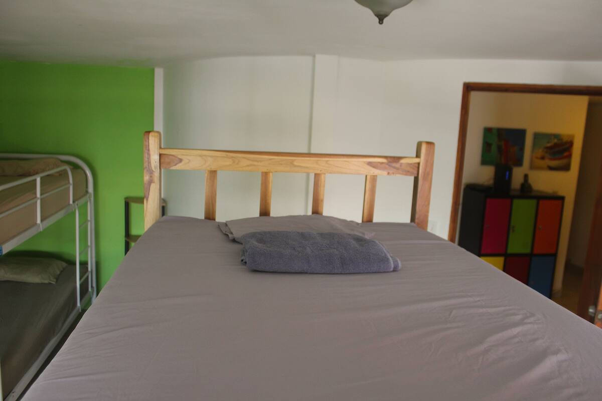 Una cama individual con cabecera de madera, colchón gris y una manta gris doblada.