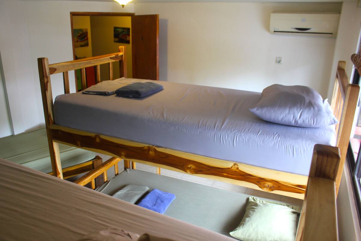 Una cama individual con estructura de madera, un almohadón y una manta.