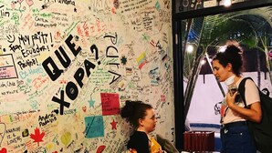 A room with a green couch, a wall covered in various writings and drawings, and a window with a view of palm trees. - Hostel Casa Areka (Panama City)