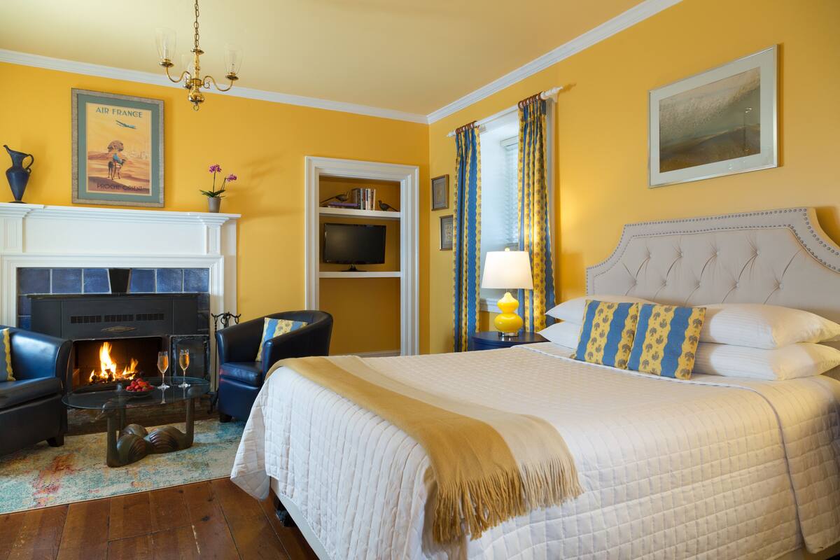 A hotel room with a fireplace, a bed with white and blue bedding, a television, and a chandelier.
