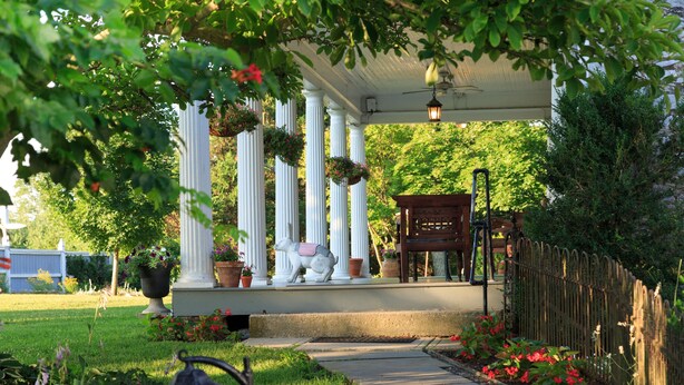 A covered porch with white columns, a bench, and hanging flower baskets. - L'Auberge Provencale Inn & Restaurant (Boyce)