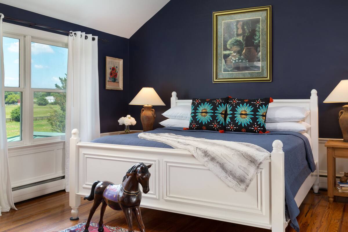 A bedroom with a bed, two bedside lamps, a window with curtains, a framed picture on the wall, and a small rug.