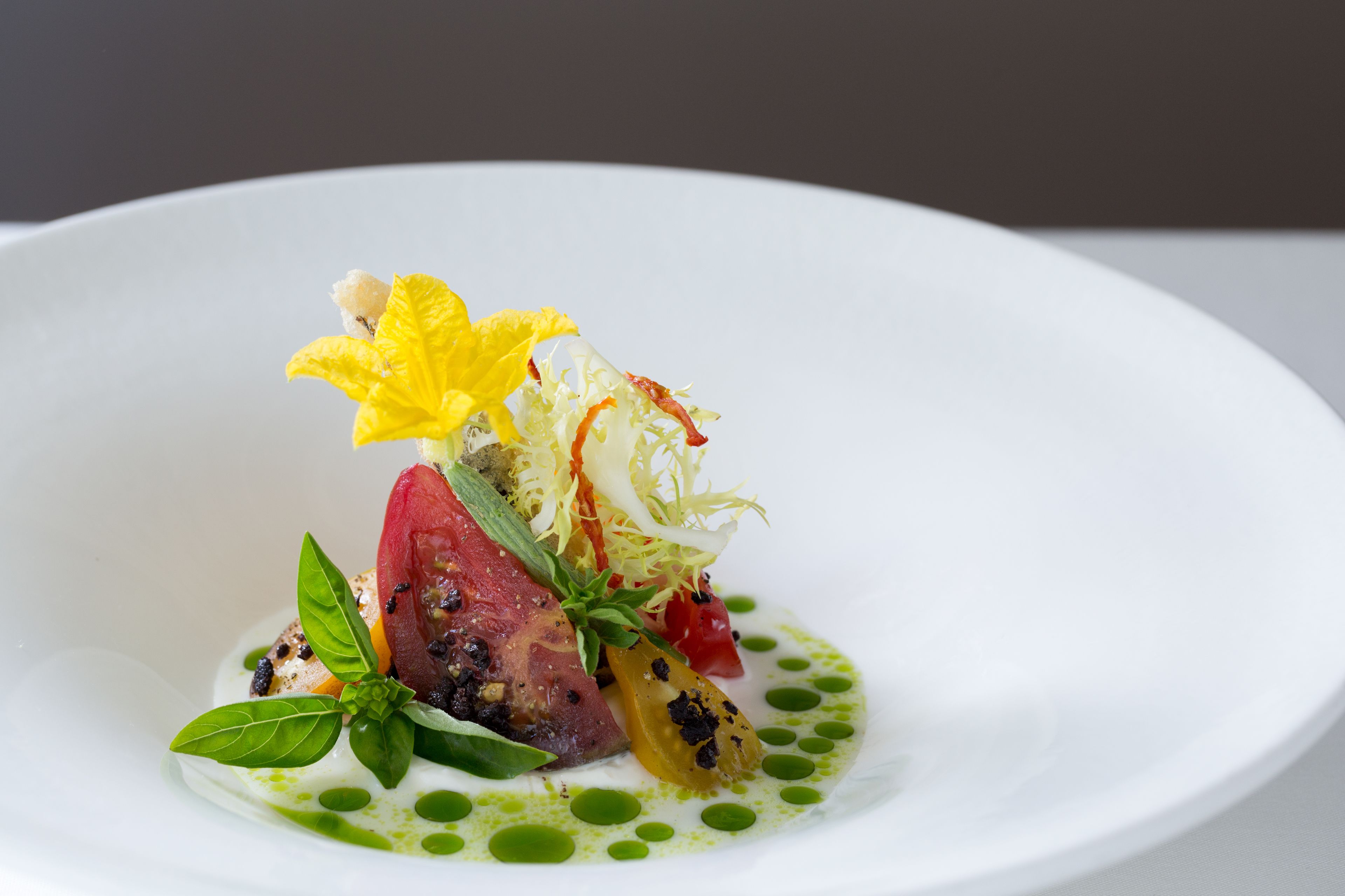 A white plate with a colorful dish of food, including a red meat component, vegetables, and a yellow flower garnish.