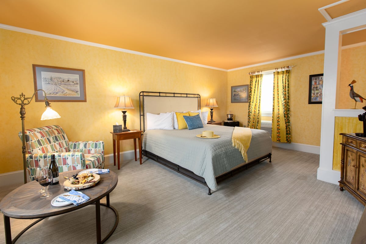 A bedroom with a bed, bedside tables, a chair, a table with a bottle of wine, and a framed picture on the wall.